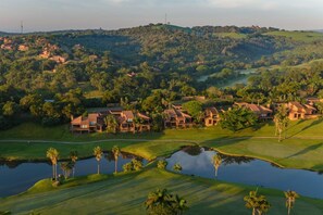 A golf course with multiple houses, a pond, and surrounding greenery. - San Lameer Villa Rentals Three Bedroom Luxury 13908 (Southbroom)
