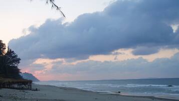 A beach with a thatched structure, calm sea, and overcast sky.