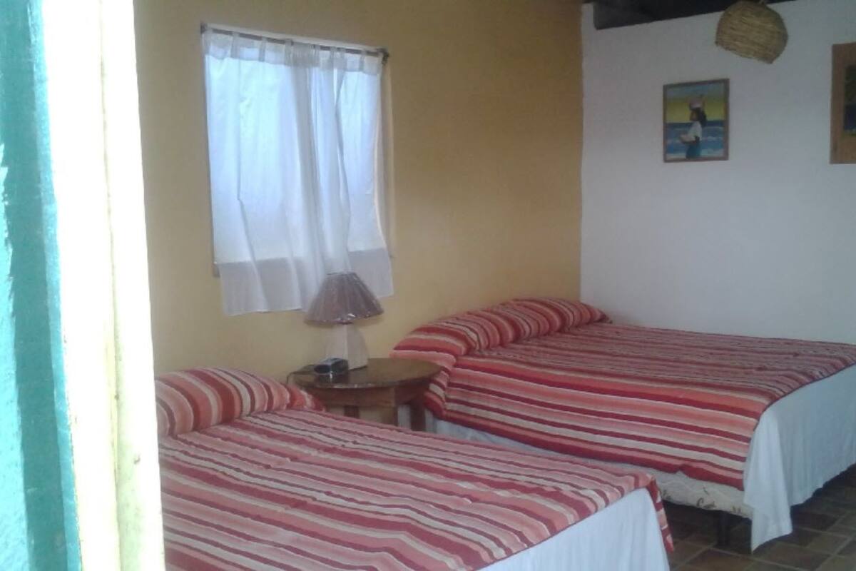 A room with two beds, a small table, a lamp, and a window with curtains.