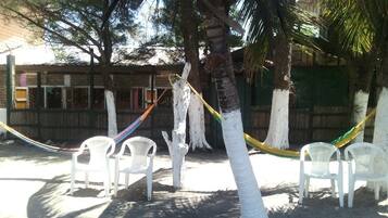 Un paisaje de playa con sillas de plástico blancas, una hamaca y una palmera.