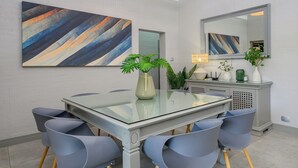 A modern dining area with a glass-top table, grey chairs, and abstract paintings on the walls. - San Lameer Villa Rentals Three Bedroom Superior 2605 (Southbroom)