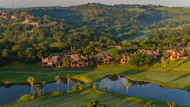 A golf course with multiple houses, a pond, and surrounding greenery. - San Lameer Villa Rentals Two Bedroom Standard 1928 (Southbroom)