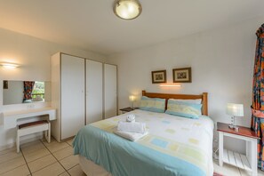 A hotel room with a bed, a desk, a wardrobe, and a nightstand. - San Lameer Villa Rentals Two Bedroom Standard 1928 (Southbroom)