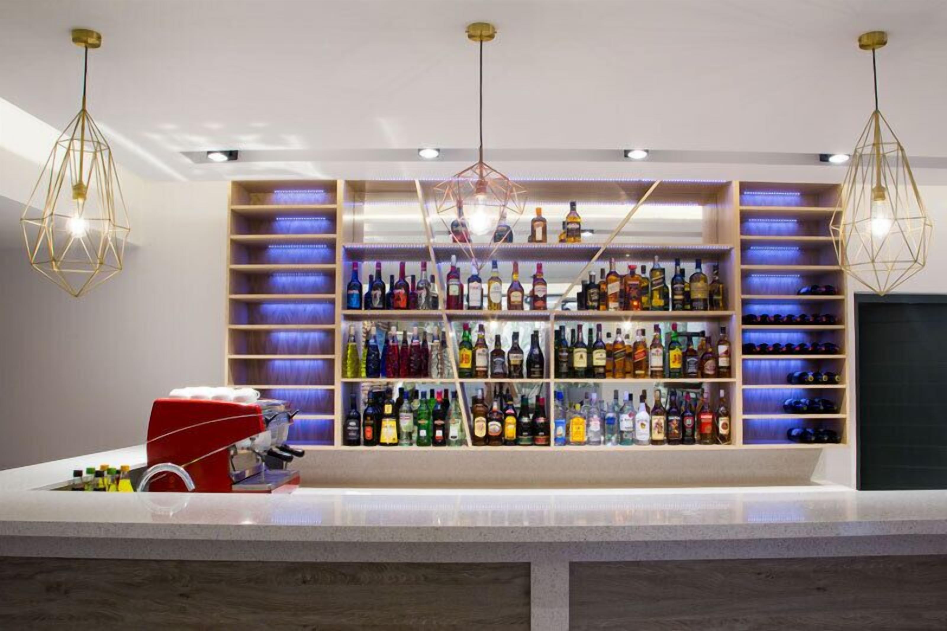 A bar area with shelves of liquor bottles, a coffee machine, and geometric pendant lights.