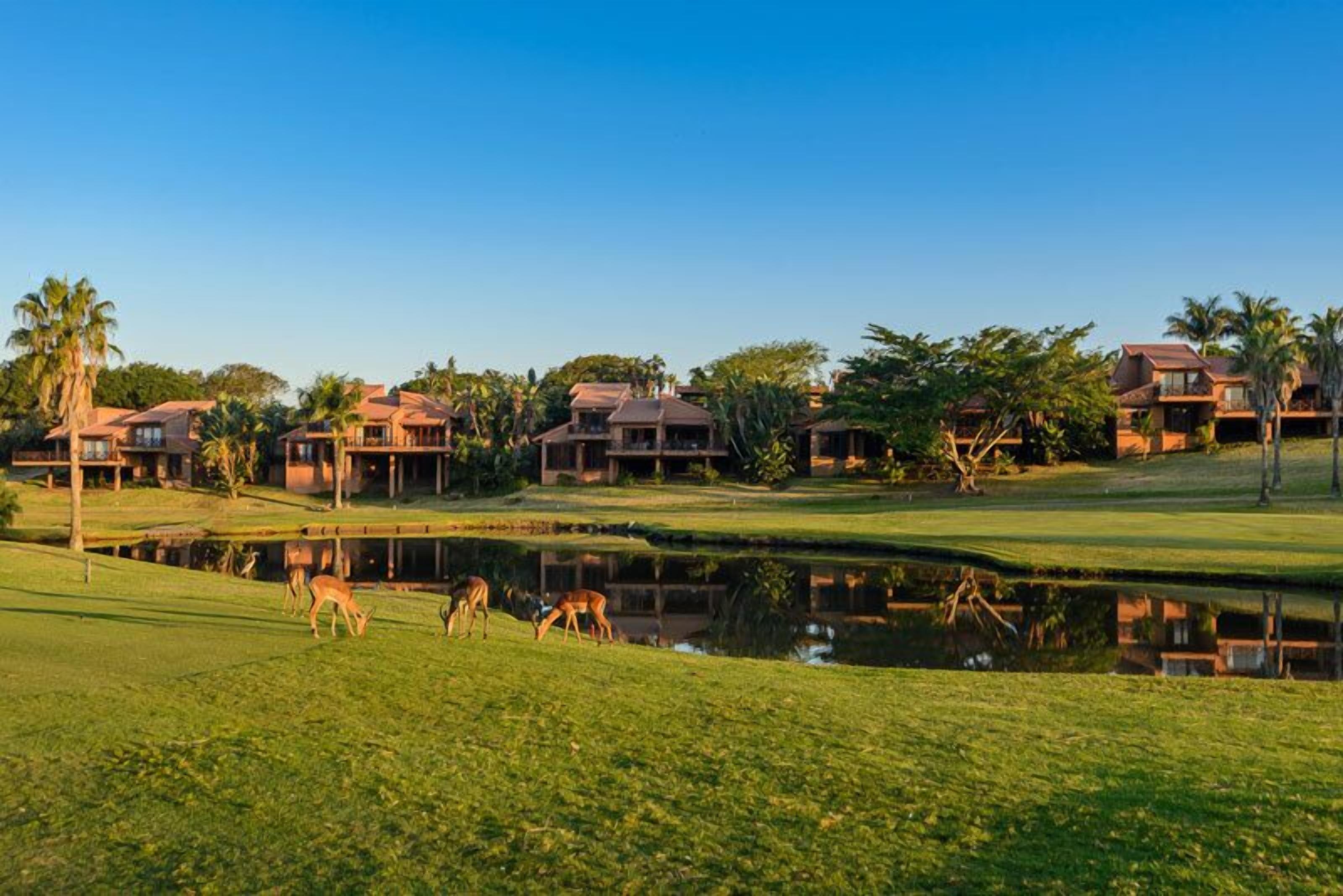 A golf course with multiple buildings, a pond, and deer grazing.