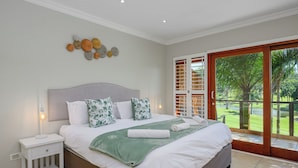 A bedroom with a large bed, a nightstand, a wall-mounted light, and a view of a golf course through a sliding glass door. - San Lameer Villa 10429 (Southbroom)