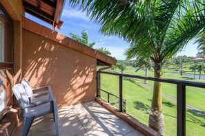 Un balcone con una sedia, vista su un campo da golf e una palma.