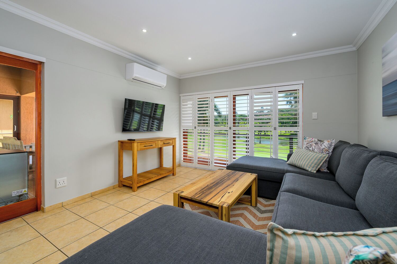 A modern living room with a grey sofa, a wooden coffee table, and a TV mounted on the wall.
