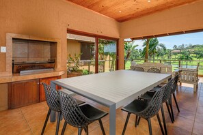 Un'area pranzo all'aperto con un tavolo grande e sedie, un barbecue integrato e vista su un giardino rigoglioso.