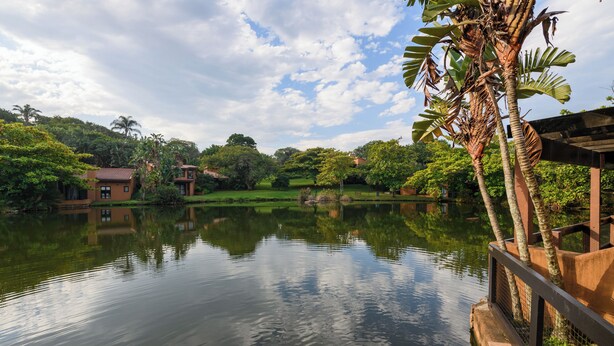 A calm lake with a wooden bridge, surrounded by lush greenery and a few buildings in the background. - San Lameer Villa Rentals 1909 (Southbroom)
