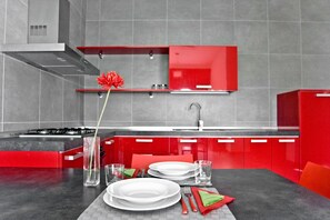 A modern kitchen with red cabinets, a gas stove, and a dining area set with plates and glasses.