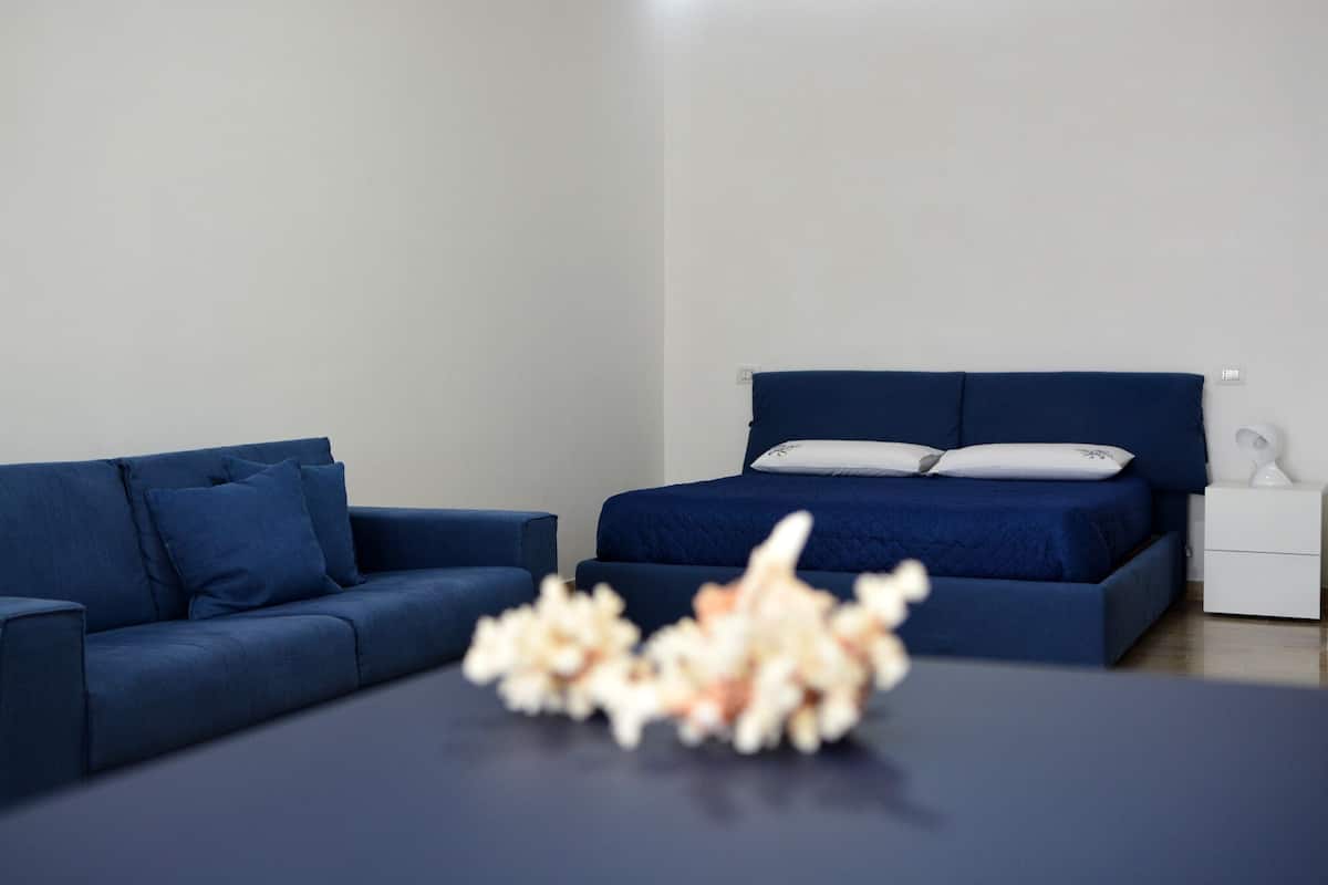 Un dormitorio moderno con un sofá azul, una cama con ropa de cama azul a juego y una mesita de noche blanca con una lámpara.
