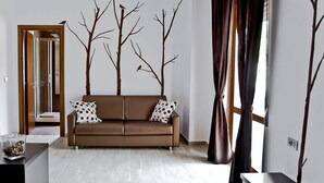 A modern living room with a brown sofa, a glass coffee table, and a decorative tree branch wall art. - InStile aparthotel (Ascea)