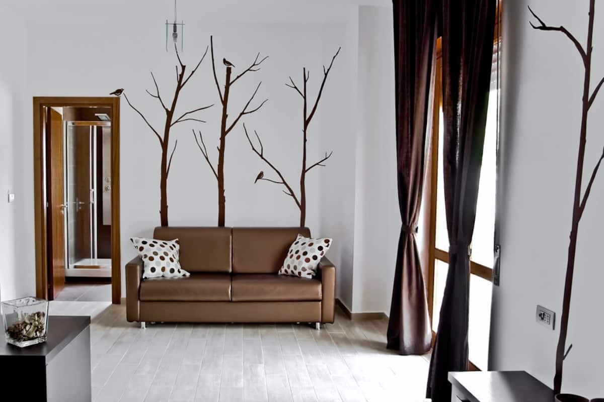 Una sala de estar moderna con un sofá marrón, una mesa de centro de vidrio y un adorno de rama de árbol en la pared.