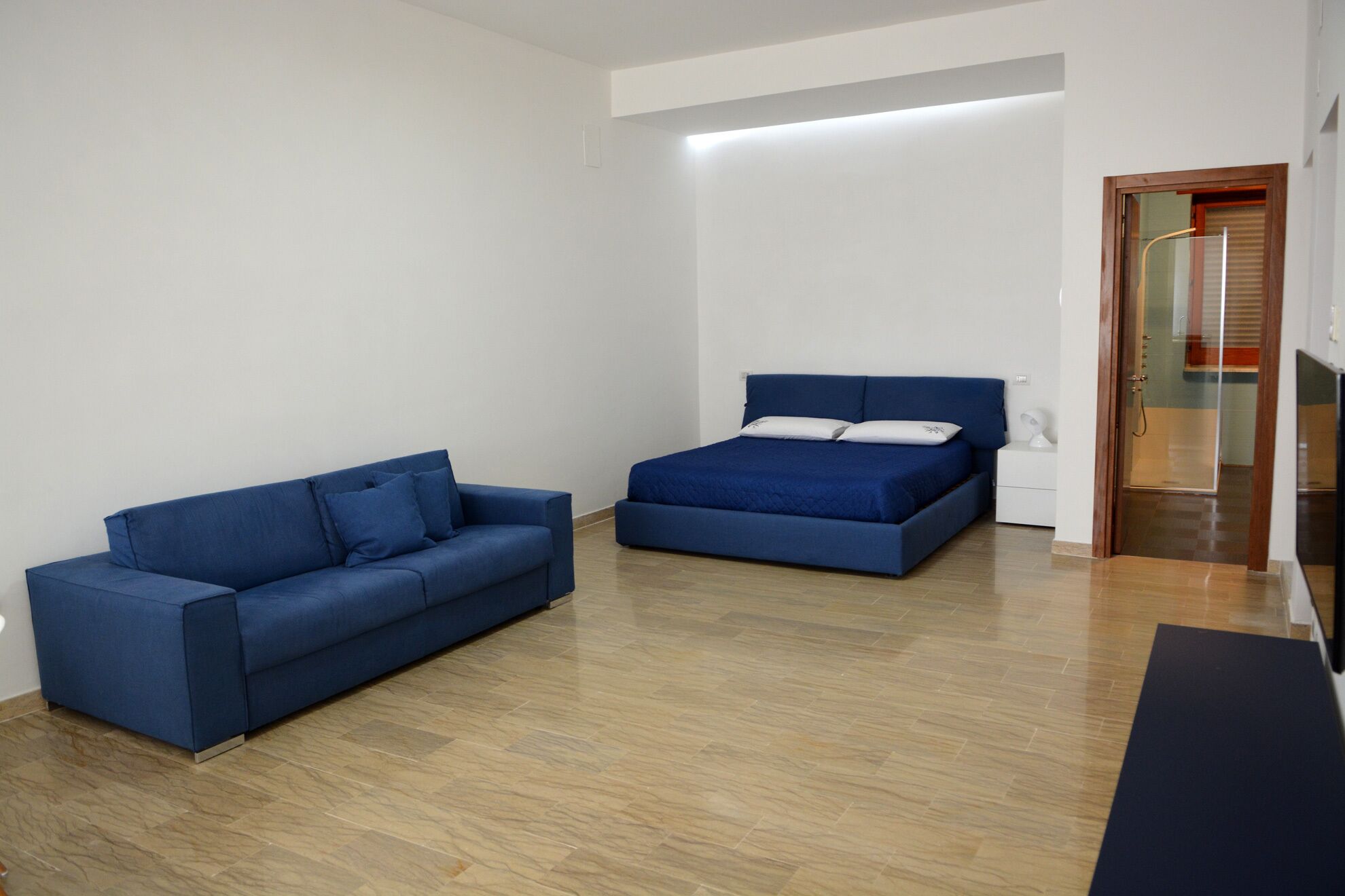 Una habitación con un sofá azul, una cama con ropa de cama azul y suelo de madera.