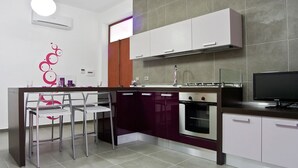 A modern kitchen with a central island, stainless steel appliances, and a flat-screen TV. - InStile aparthotel (Ascea)