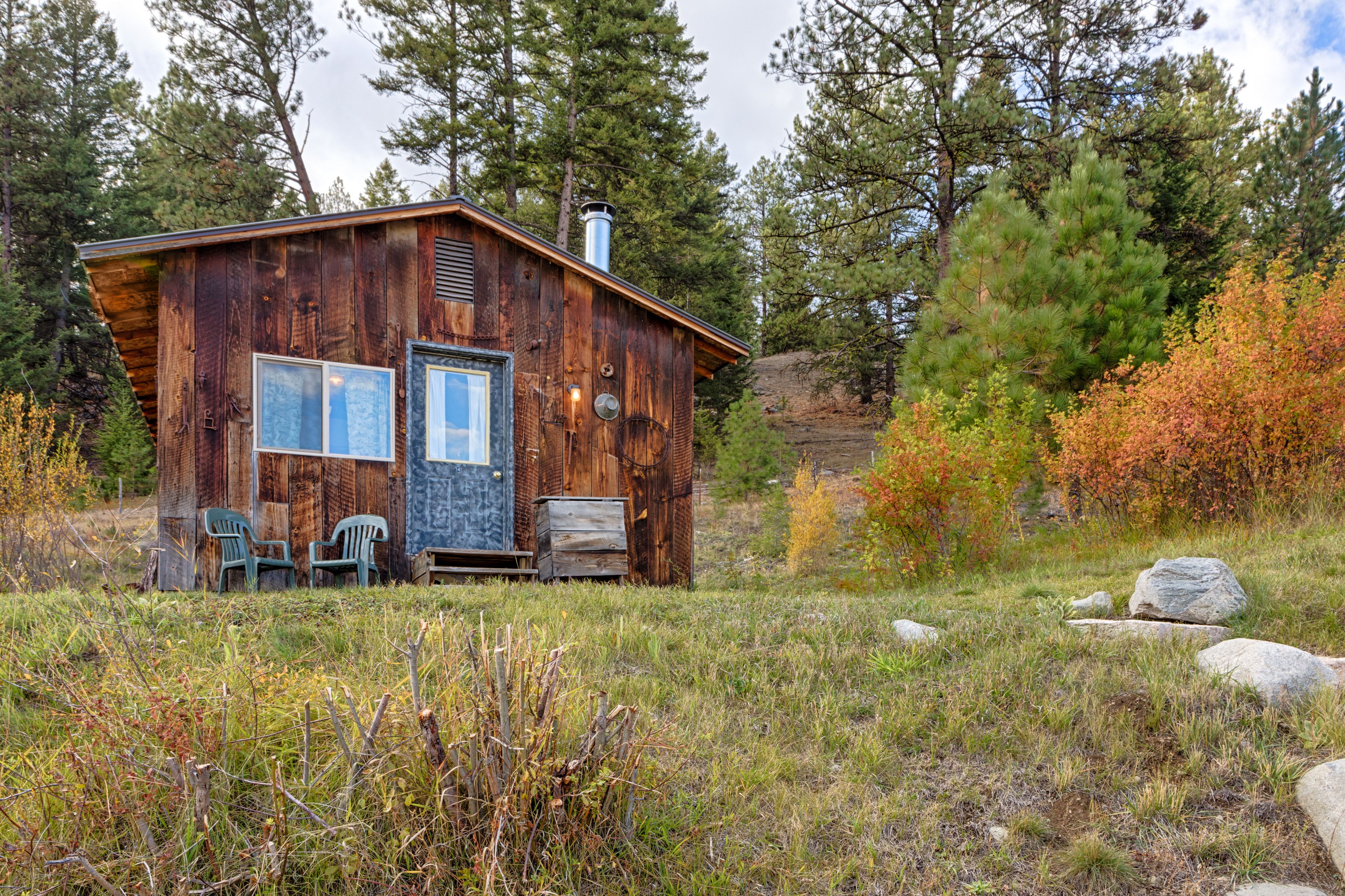 A rustic cabin with a wooden exterior, a front door, and two chairs outside.