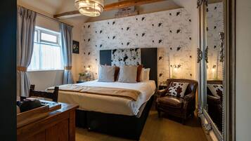 A bedroom with a large bed, a wooden dresser, a leather armchair, and a mirror.