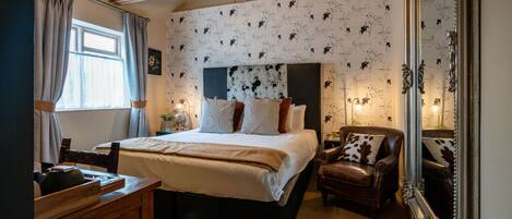 Un dormitorio con una cama grande, un aparador de madera, un sillón de cuero y un espejo.
