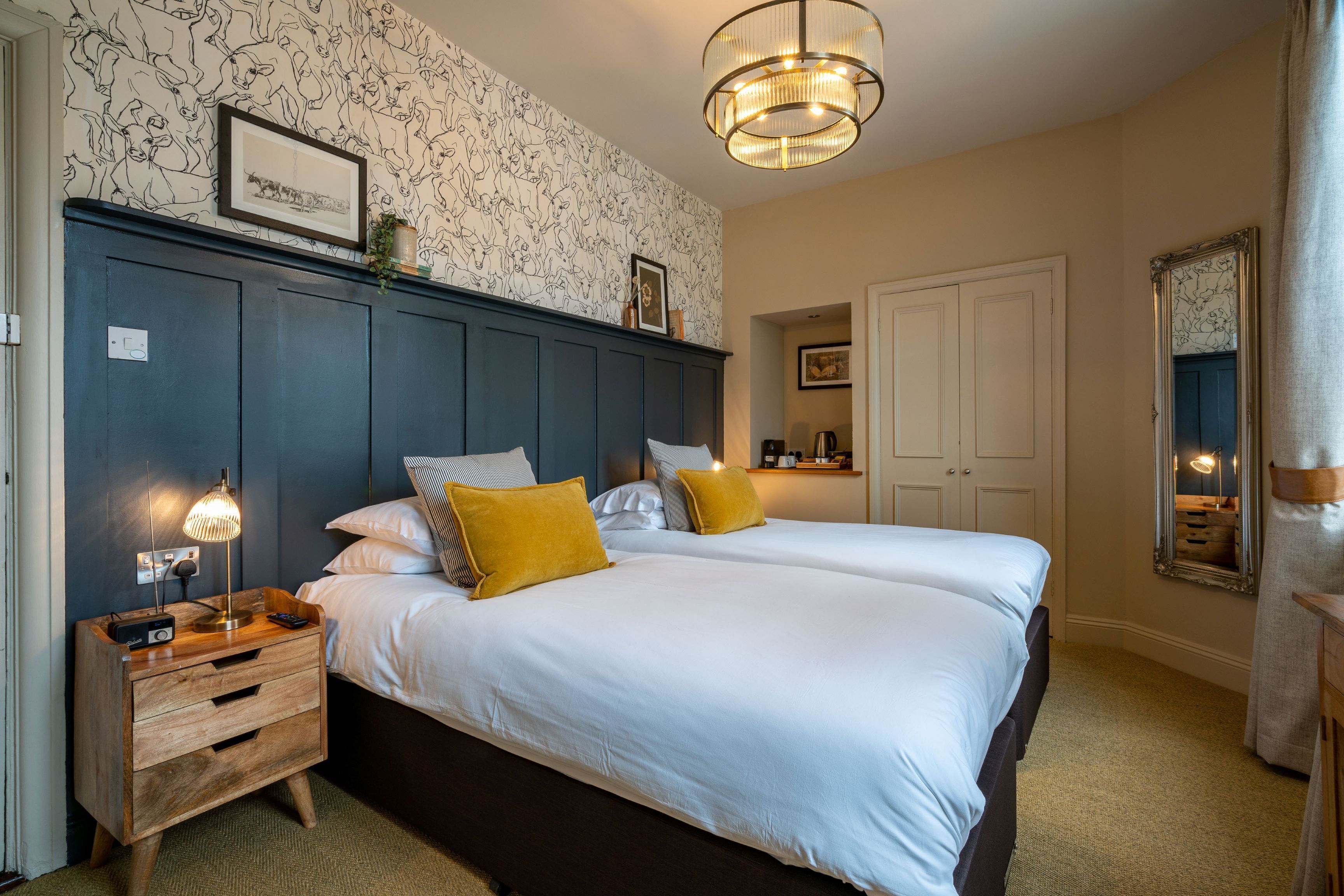 A bedroom with two beds, a nightstand with a lamp, a dresser, and a large mirror.