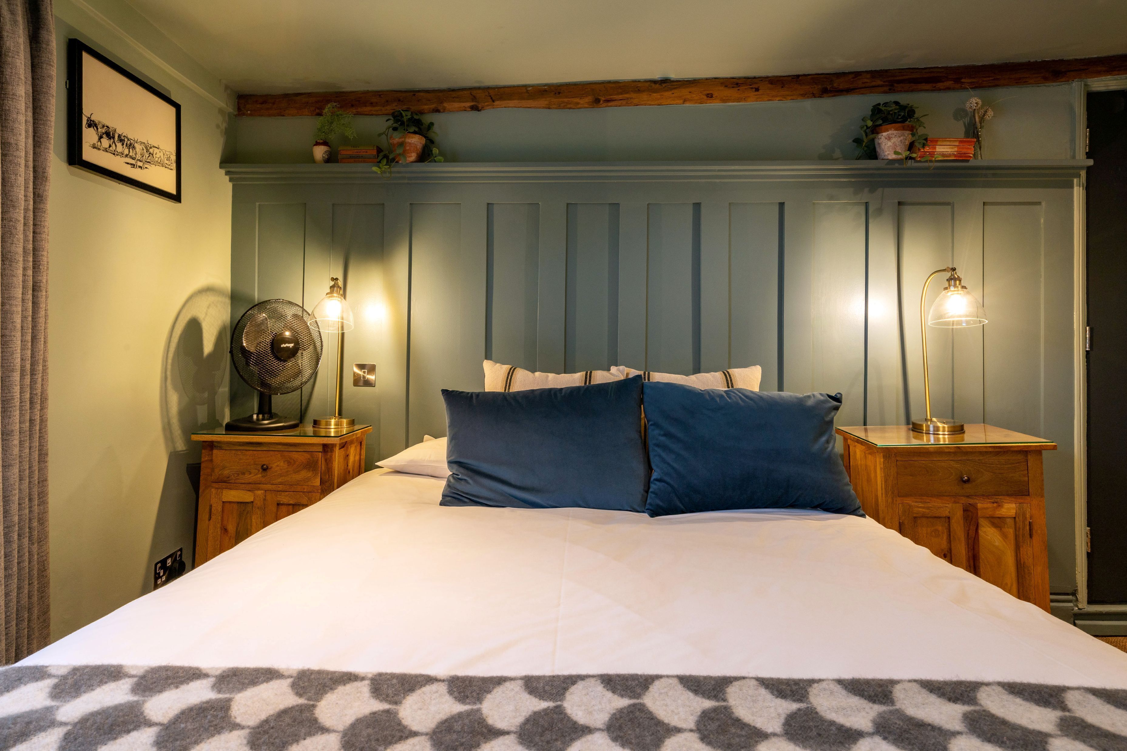 A bedroom with a bed, two bedside tables, a wall-mounted fan, and a wall-mounted lamp.