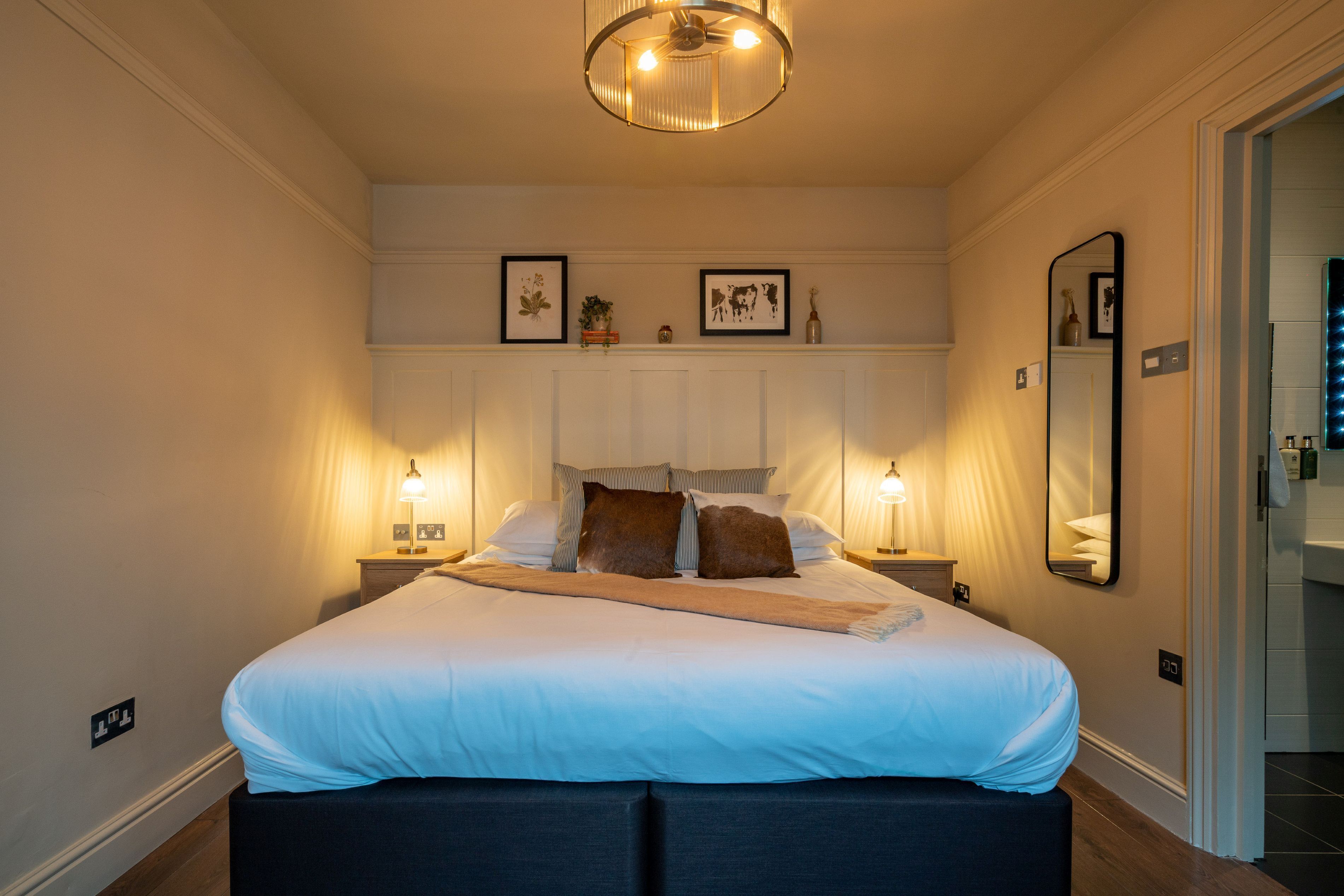 A neatly made bed with a headboard, bedside tables with lamps, and framed pictures on the wall.