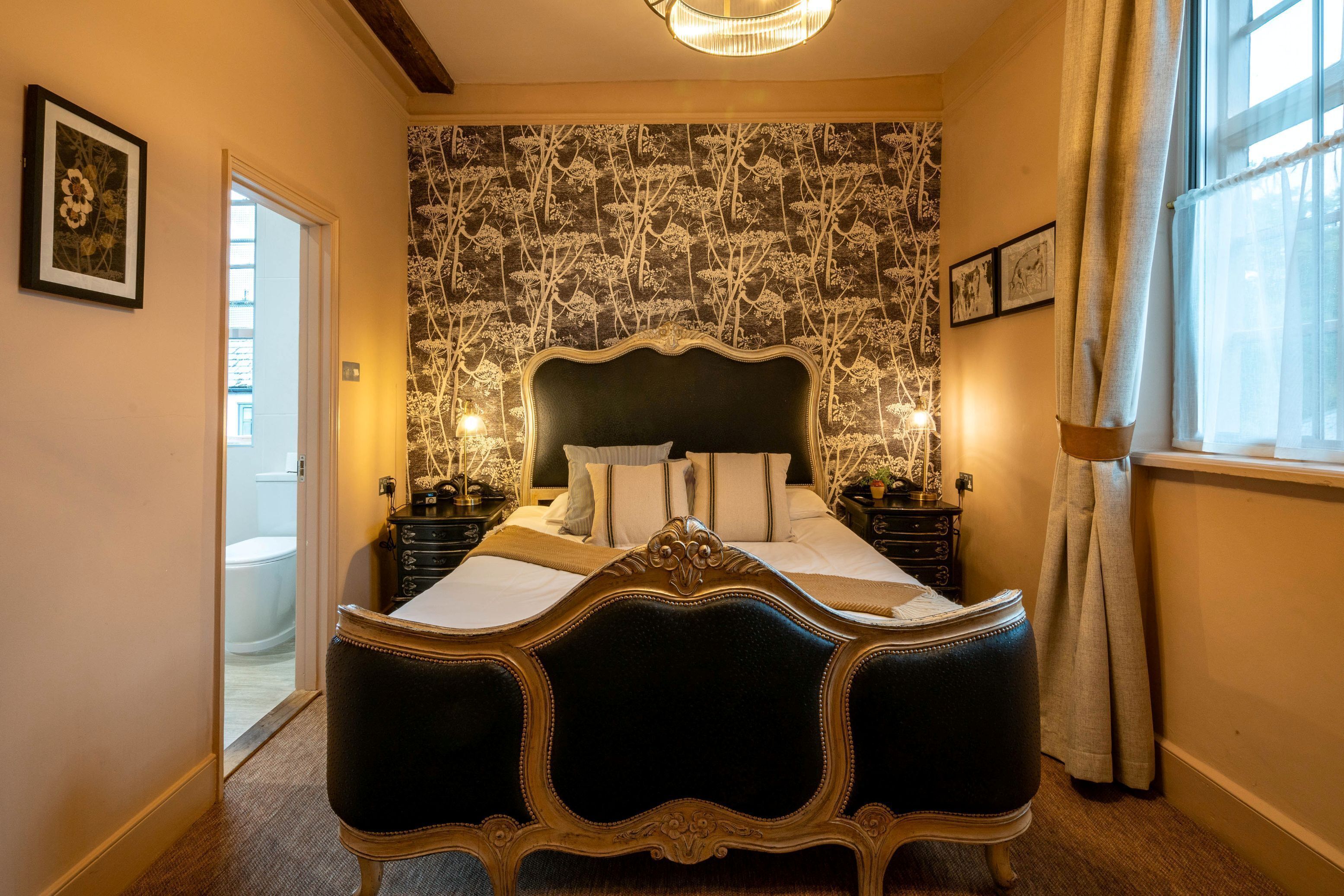 A bedroom with a large bed, a patterned wallpaper, and a window with curtains.
