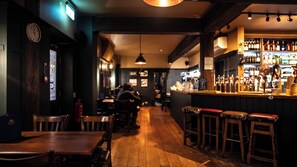 A bar with wooden furniture, a clock on the wall, and a bar counter with bottles. - The Bull Inn (Bury St Edmunds)