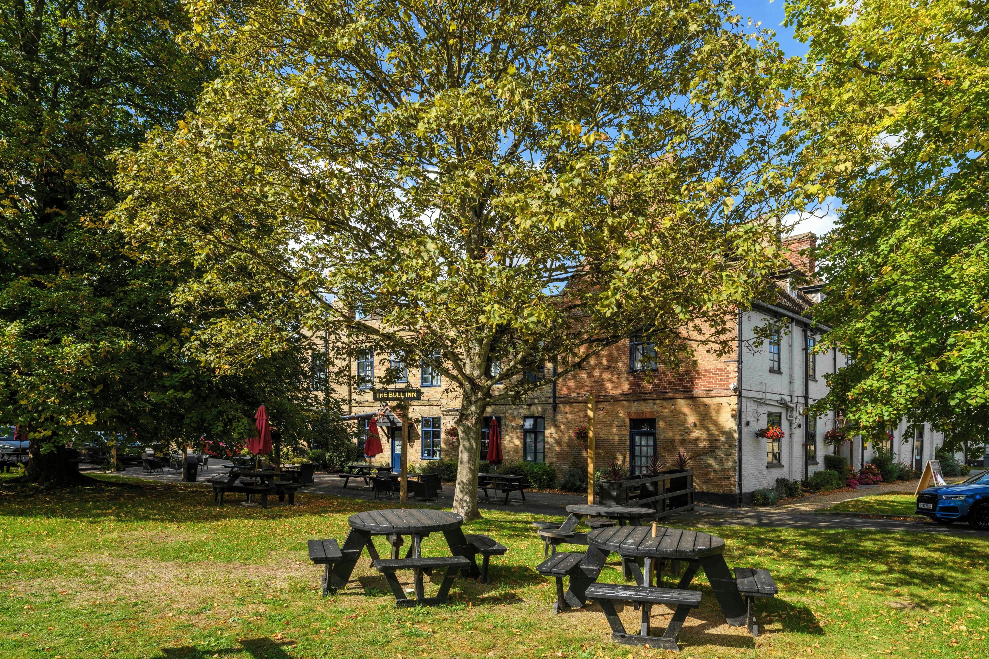 Un parc avec des tables de pique-nique, un bâtiment portant l’inscription « The Bull Inn », et un arbre qui offre de l’ombre.