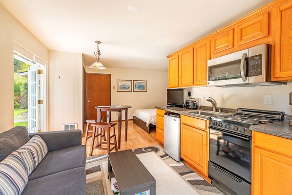 A compact kitchen with wooden cabinets, a microwave, a dishwasher, and a stove. - Brinnon Gardens (Brinnon)