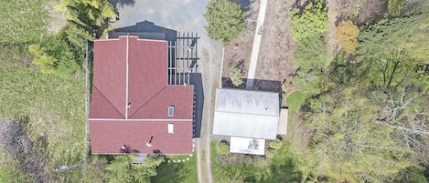 An aerial view of a property with a red-roofed building, a smaller adjacent structure, and surrounding greenery.