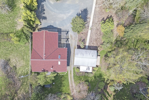 An aerial view of a property with a red-roofed building, a smaller adjacent structure, and surrounding greenery.