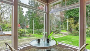 A conservatory with a glass table, two chairs, and a view of a garden. - Brinnon Gardens (Brinnon)