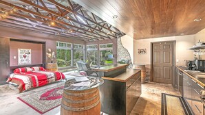 A spacious room with a large bed, a wooden barrel, a desk with a computer, and a kitchen area. - Brinnon Gardens (Brinnon)