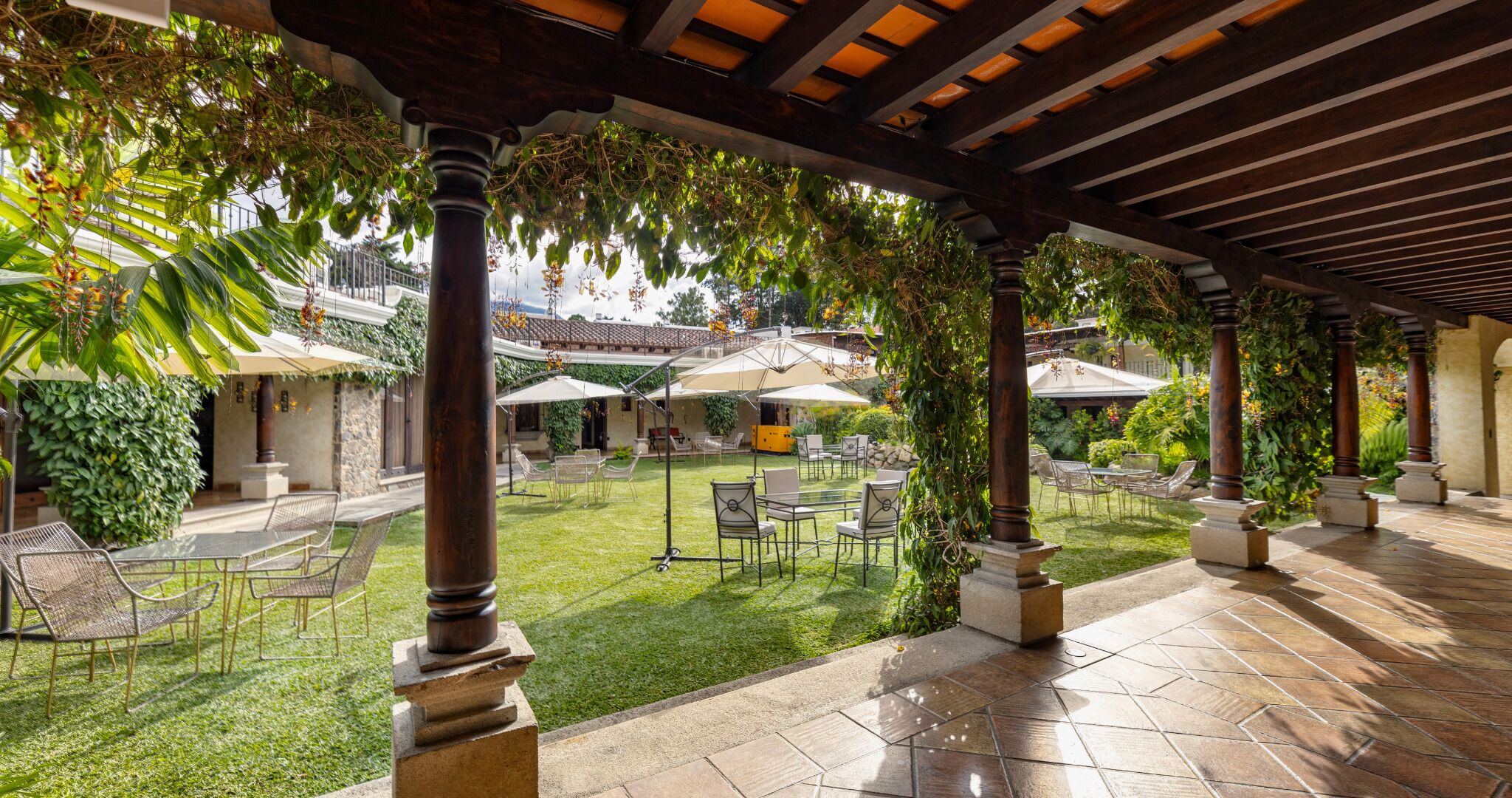 An outdoor patio area with a pergola, seating arrangements, and greenery.