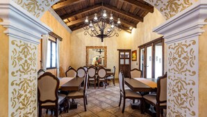 A dining area with a high wooden ceiling, a chandelier, and patterned wallpaper. - Casa Faustina Boutique Hotel (Antigua Guatemala)