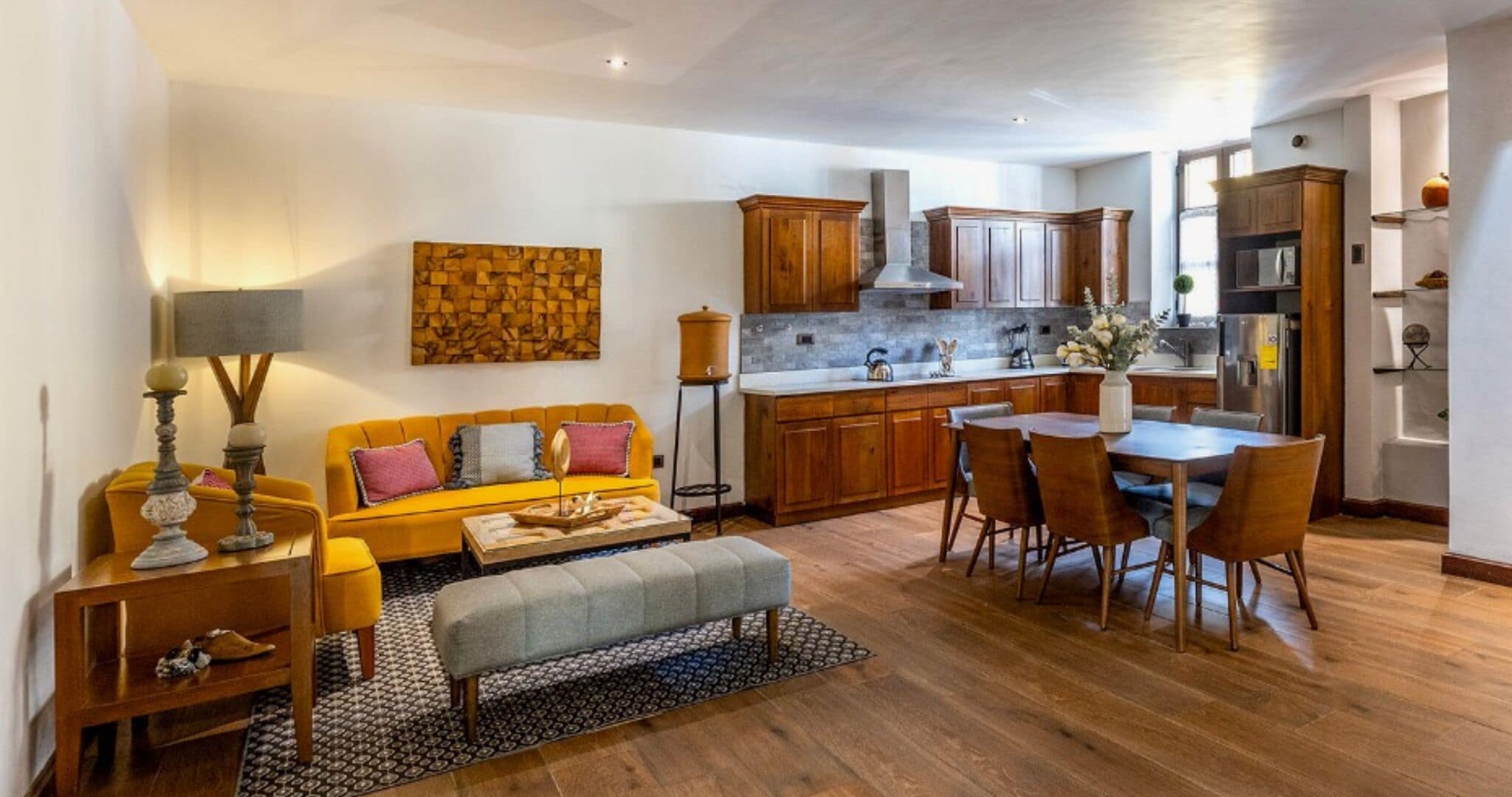 A modern kitchen with wooden cabinets, a dining area with a table and chairs, and a living room with a sofa and a coffee table.