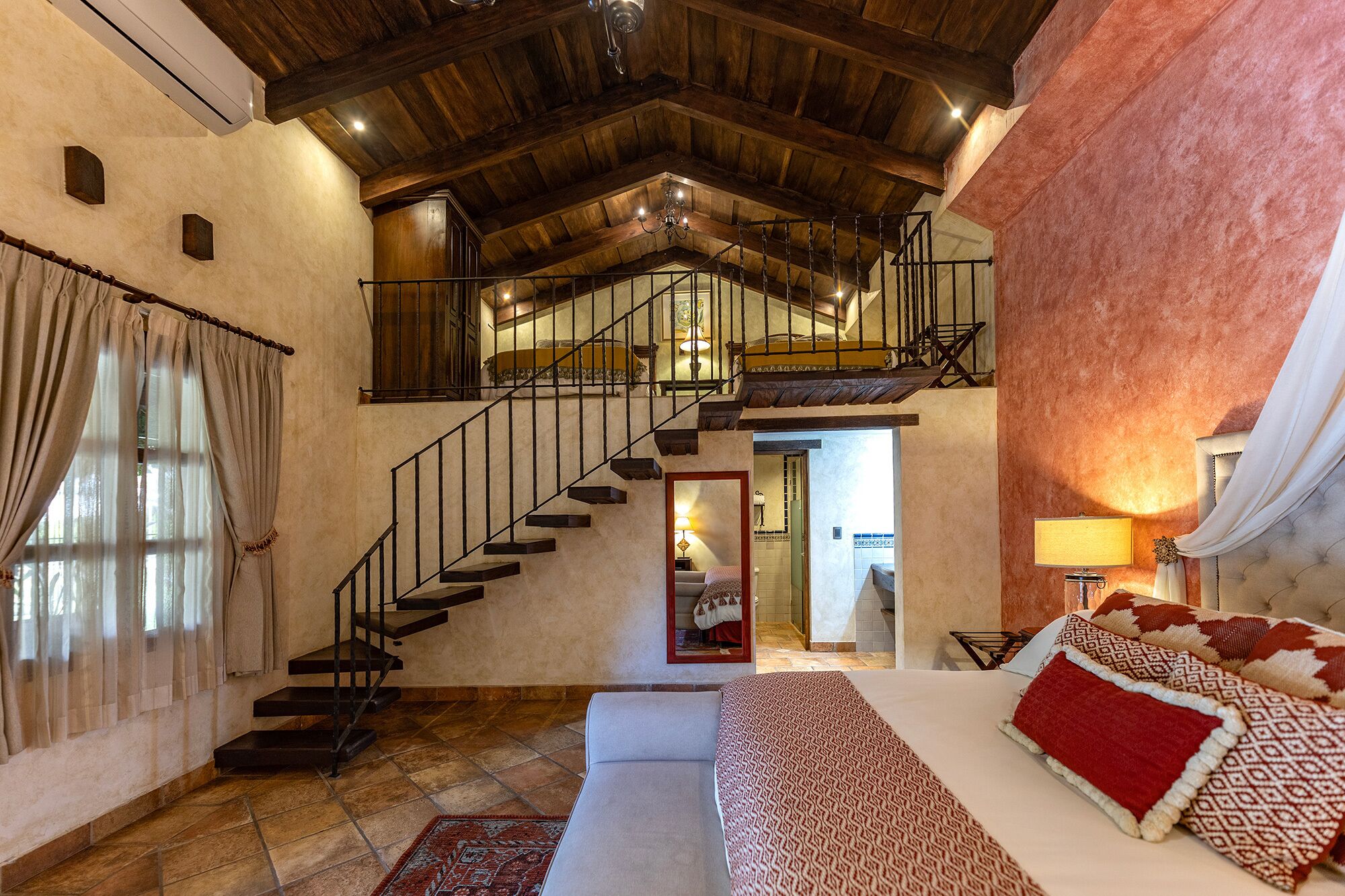 A bedroom with a large bed, a staircase, and a view of a bathroom.