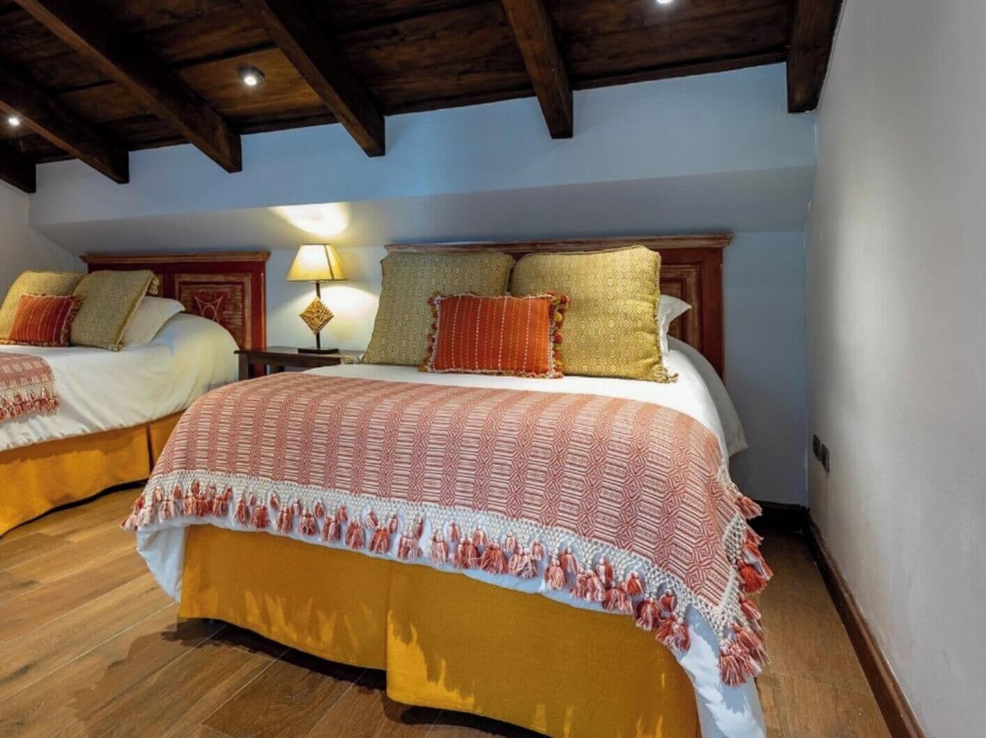 A hotel room with two beds, wooden flooring, and a ceiling with exposed beams.