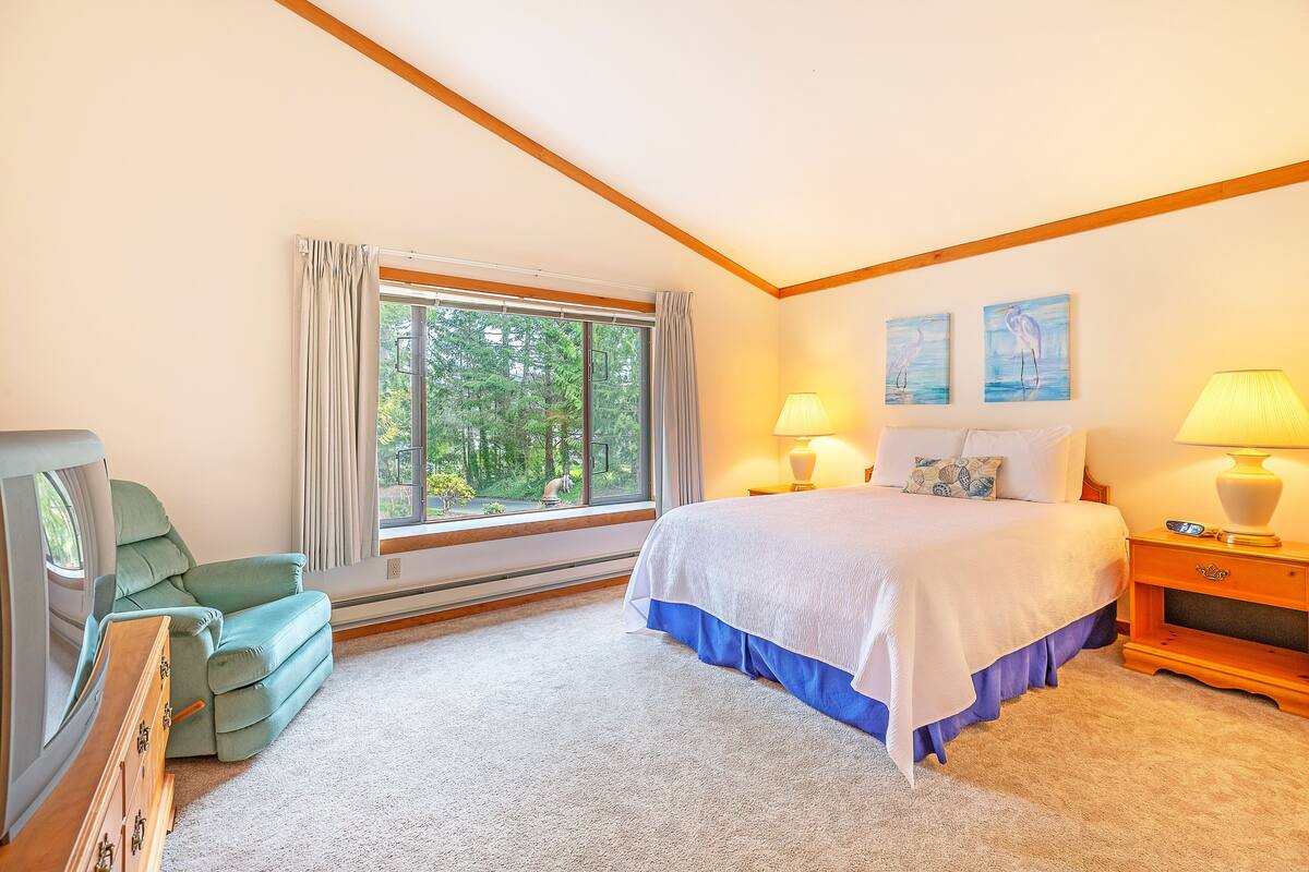 A bedroom with a bed, two bedside lamps, a nightstand, a dresser, and a window with curtains.