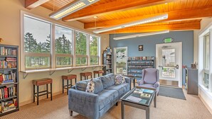 A cozy reading area with a blue sofa, wooden bookshelves, and a large window offering a view of trees. - Blue Heron Holidays (Union)