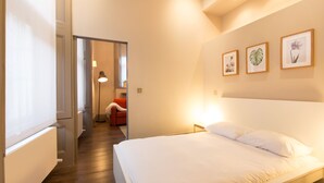 A bedroom with a large bed, a red chair, and framed botanical prints on the wall. - Emperors Gate Residence by Allô Housing (London)