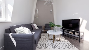 A modern living room with a grey sofa, a TV on a black stand, a white coffee table, and a patterned rug. - Emperors Gate Residence by Allô Housing (London)