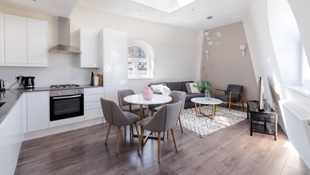 A modern kitchen with white cabinets, a gas stove, and a skylight. There is a dining area with a round table and chairs. - Emperors Gate Residence by Allô Housing (London)