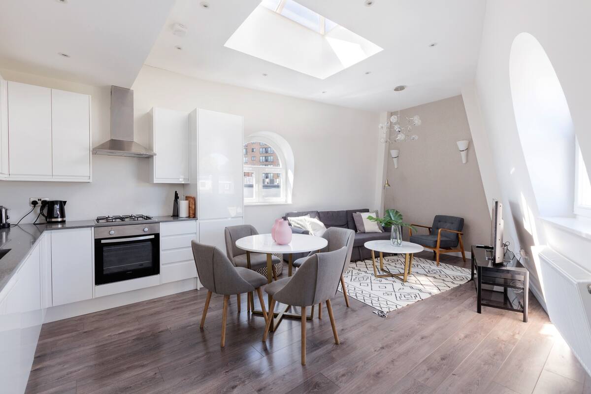 A modern kitchen with white cabinets, a gas stove, and a skylight. There is a dining area with a round table and chairs.
