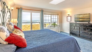 A bedroom with a large bed, a dresser, a desk, and a view of the beach. - Sweet Caroline Inn (Ocean Shores)