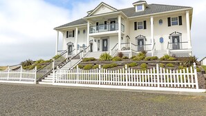 A large, two-story house with a white exterior, multiple windows, and a white picket fence. - Sweet Caroline Inn (Ocean Shores)