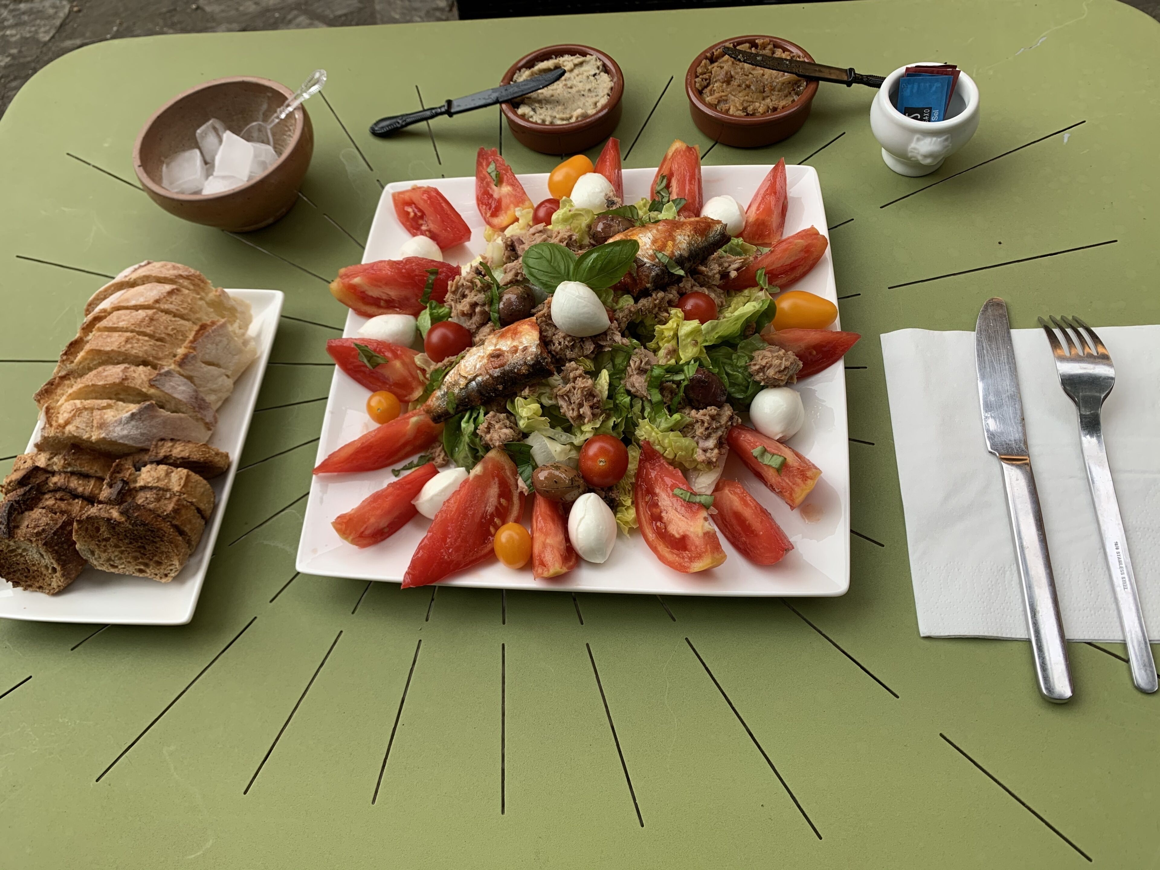 Eine Mahlzeit mit Brot, Salat und Schalen mit Beilagen auf einem grünen Tisch.