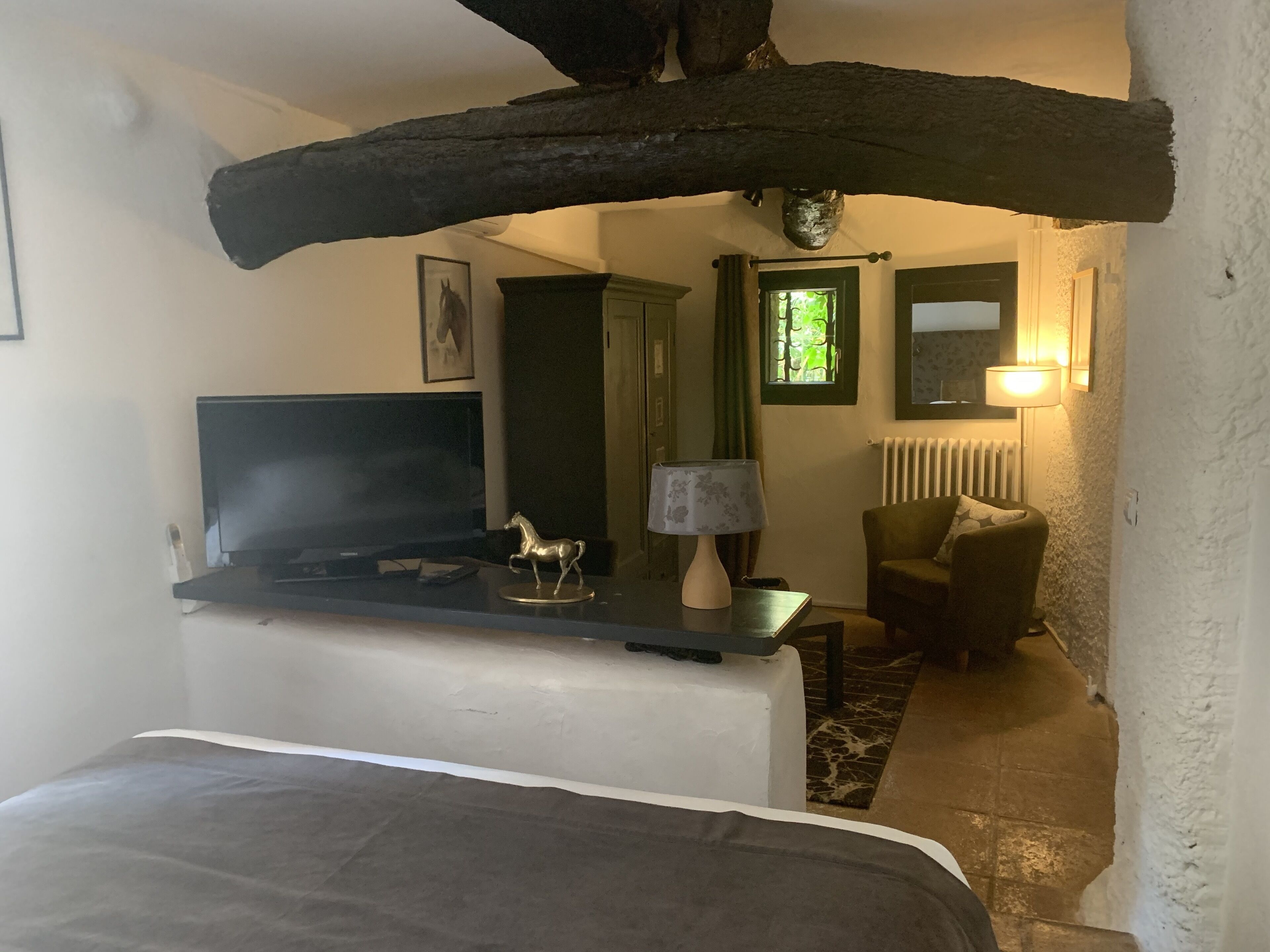 Et hyggeligt værelse med en seng, et skrivebord med tv, en lampe og en stol.