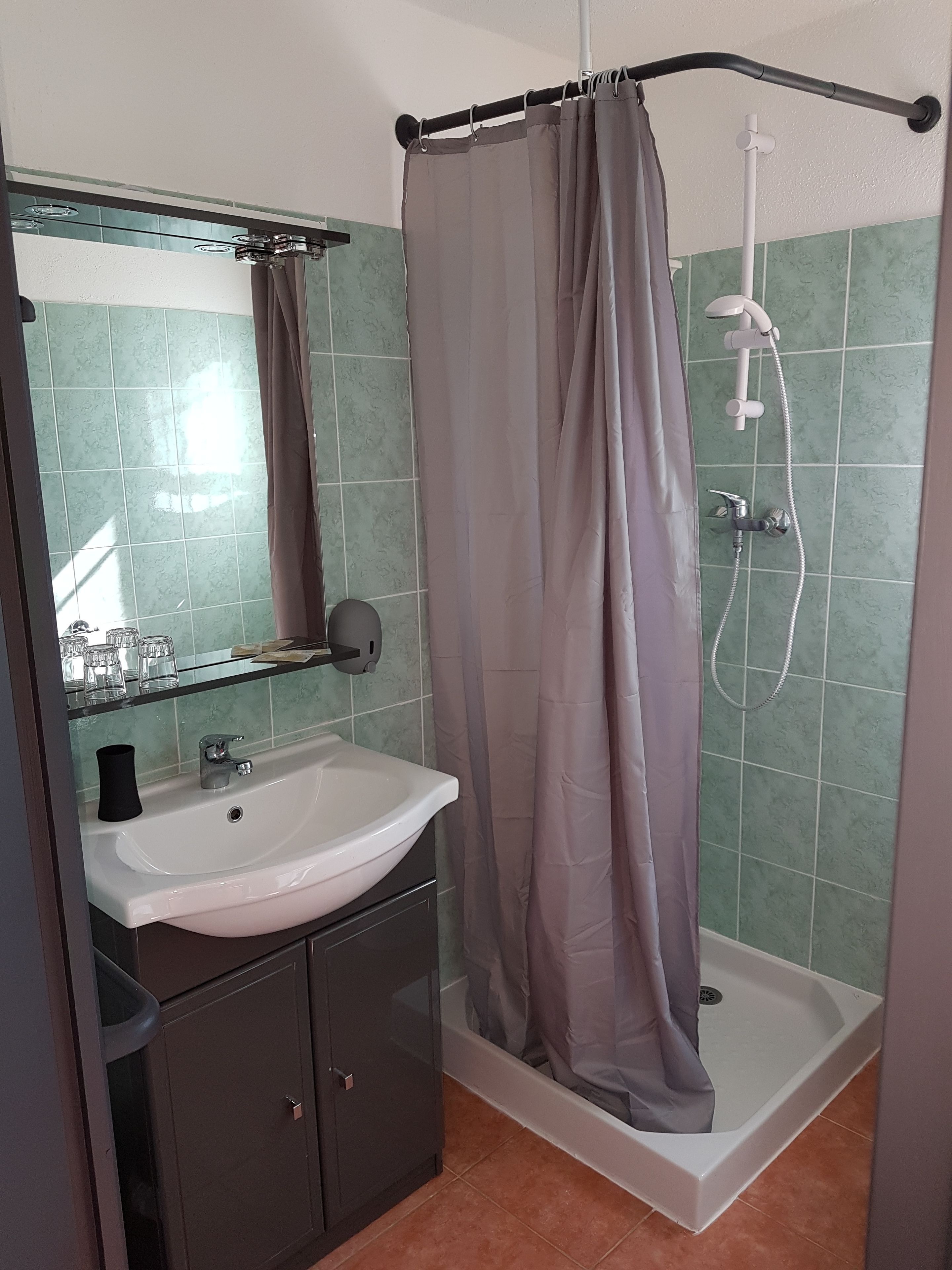 A bathroom with a white sink, a glass cabinet, a shower with a curtain, and green tiled walls.